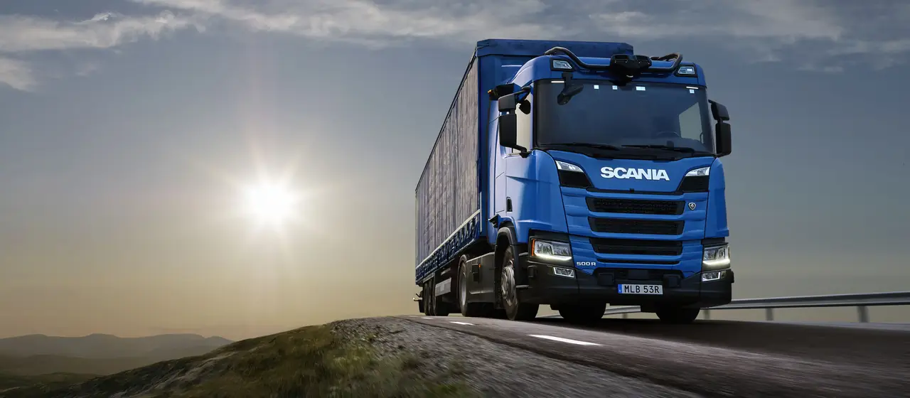 Caminhão Scania azul com carreta em uma estrada ao pôr do sol